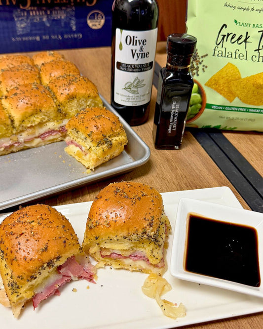 Baked corned beef sliders on Hawaiian rolls with provolone, caramelized onion jam, and Black Walnut Balsamic, served warm on a white plate.