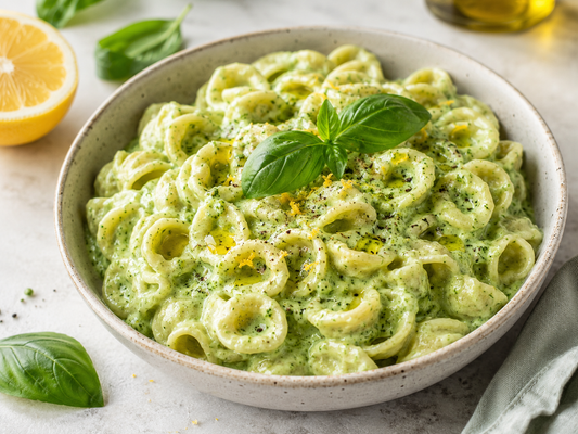 Bowl of creamy basil avocado pasta made with orecchiette, garnished with fresh basil, lemon zest, cracked black pepper, and a drizzle of olive oil.