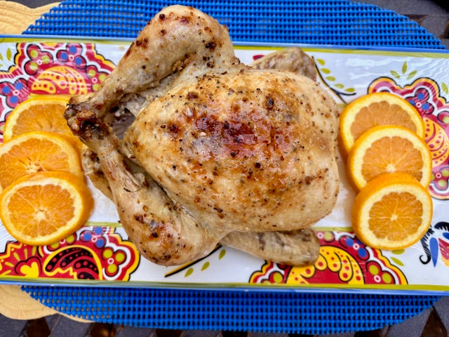 Roasted whole chicken seasoned with Garlic Chili Olive Oil and Lime Pepper Blend, served on a colorful platter with fresh orange slices.