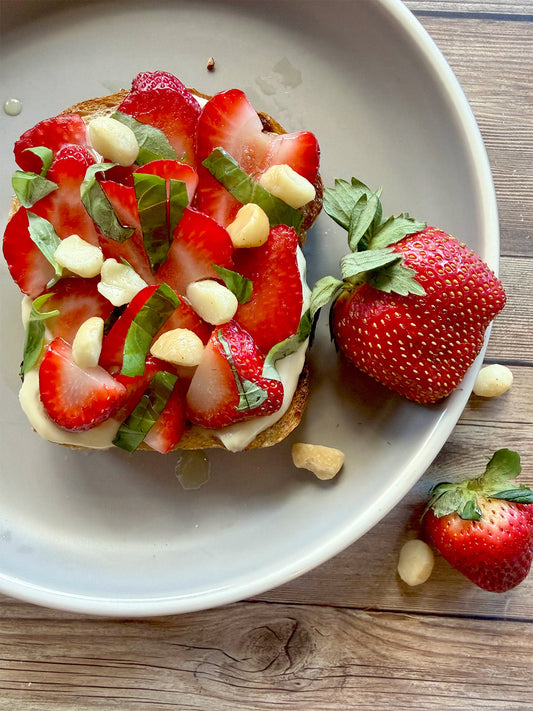 Strawberry basil ricotta toast with sliced strawberries, chopped basil, macadamia nuts, and balsamic drizzle on a plate.