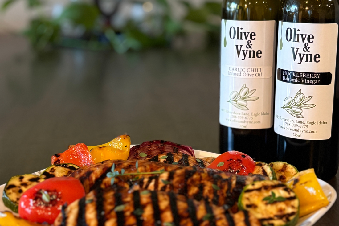 Grilled chicken and summer vegetables plated in front of Olive and Huckleberry Balsamic and Garlic Chili Olive Oil bottles