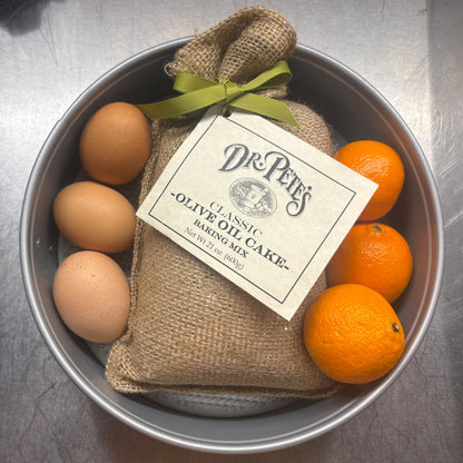 Dr. Pete’s Classic Olive Oil Cake Baking Mix displayed with eggs and fresh oranges in a cake pan.